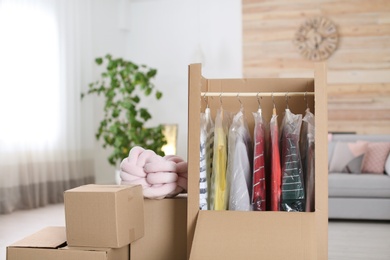 Cardboard wardrobe box with clothes on hangers in living room