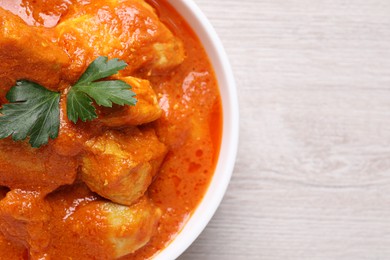 Photo of Bowl of delicious chicken curry on white wooden table, top view. Space for text