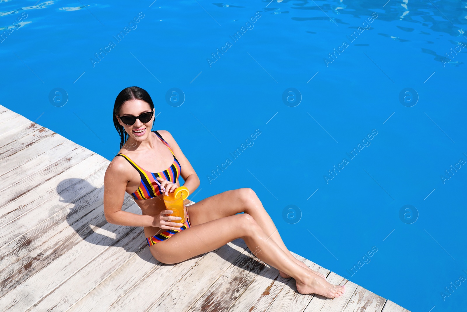 Photo of Beautiful young woman in bikini with refreshing cocktail near swimming pool on sunny day. Space for text