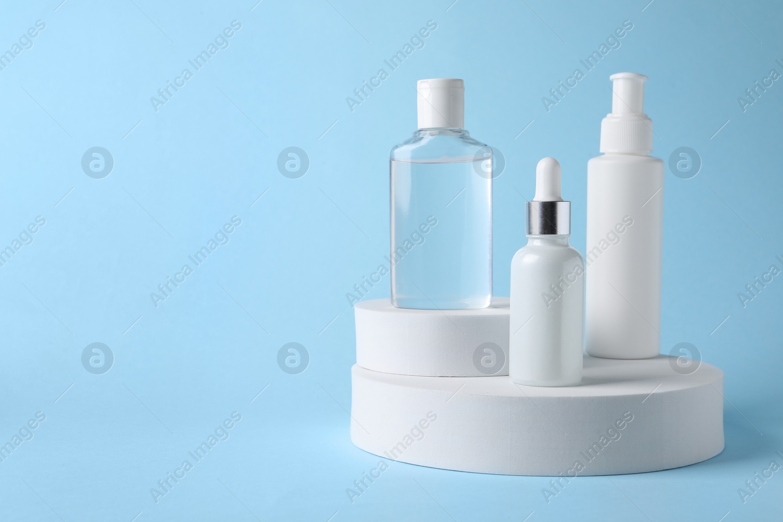 Photo of Presentation of bottles with cosmetic serums on light blue background, space for text