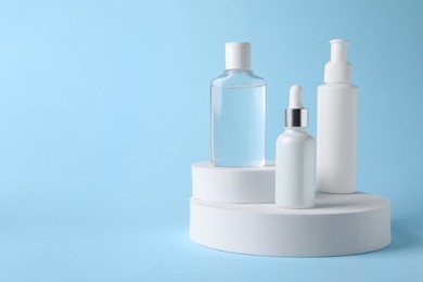 Presentation of bottles with cosmetic serums on light blue background, space for text