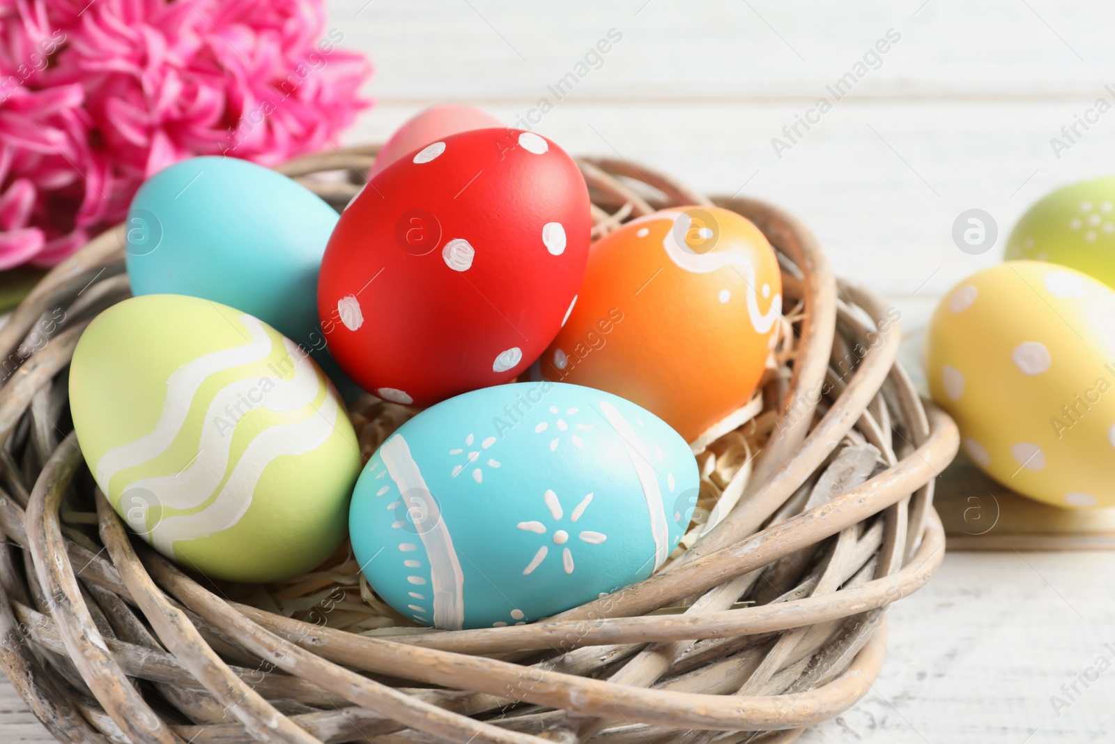 Photo of Wicker nest with colorful painted Easter eggs on table, closeup