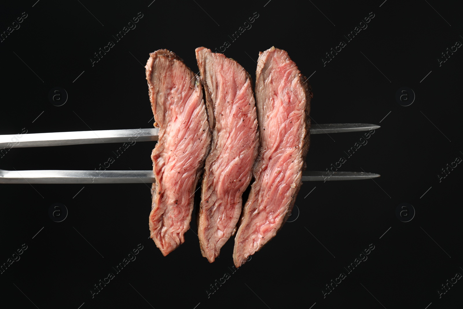 Photo of Meat fork with grilled beef pieces on black background, closeup