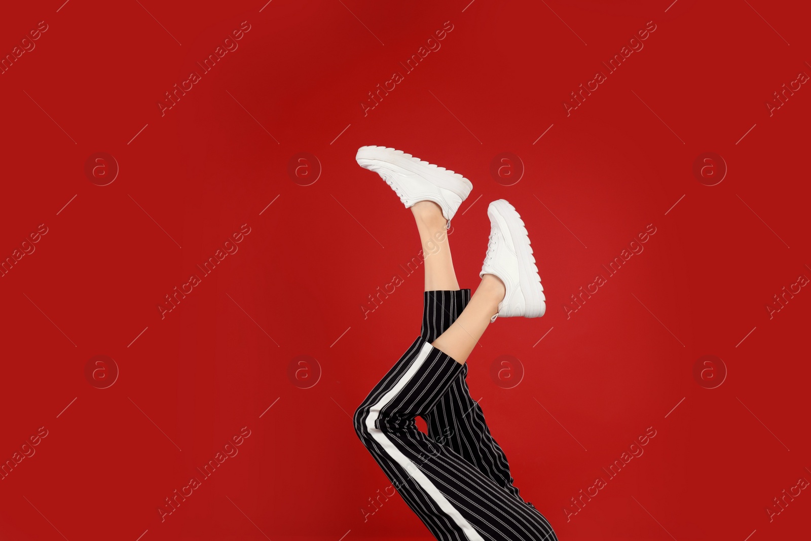 Photo of Woman in stylish sport shoes on red background