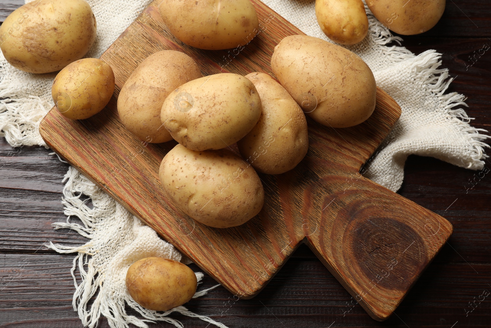 Photo of Raw fresh potatoes and cutting board on wooden table, top view