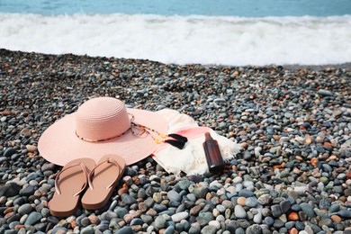 Photo of Beautiful hat, sunscreen and flip flops on pebble beach near sea