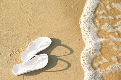 Photo of White flip flops on sand near sea, space for text. Beach accessories