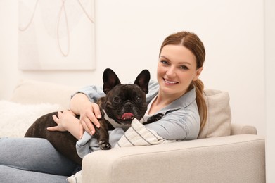 Happy woman hugging cute French Bulldog on sofa in room