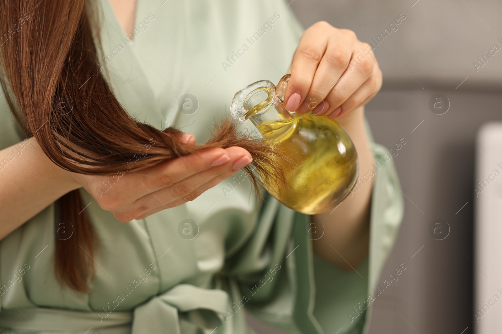 Photo of Woman applying oil hair mask onto ends at home, closeup