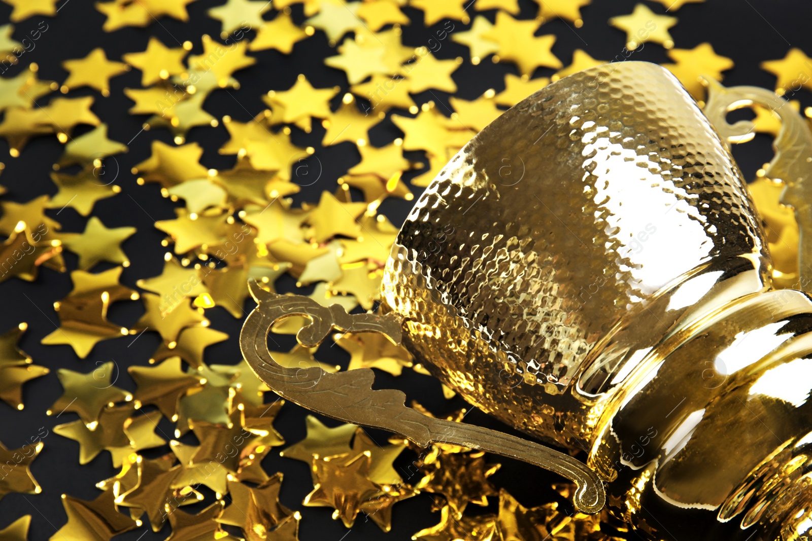 Photo of Gold trophy cup and confetti on black background, closeup. Space for text