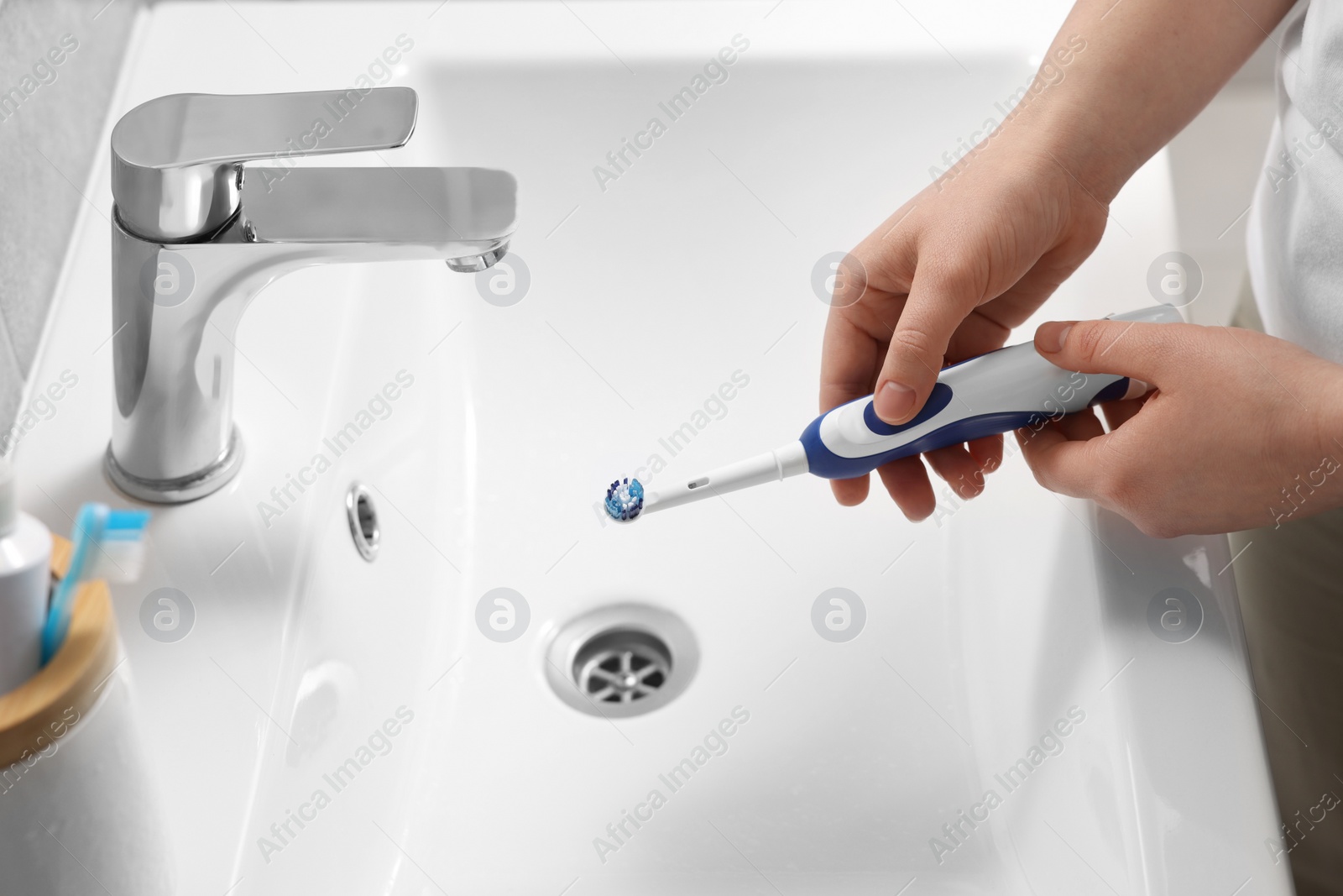 Photo of Woman holding electric toothbrush above sink in bathroom, closeup