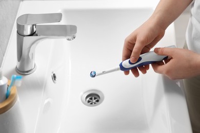 Woman holding electric toothbrush above sink in bathroom, closeup