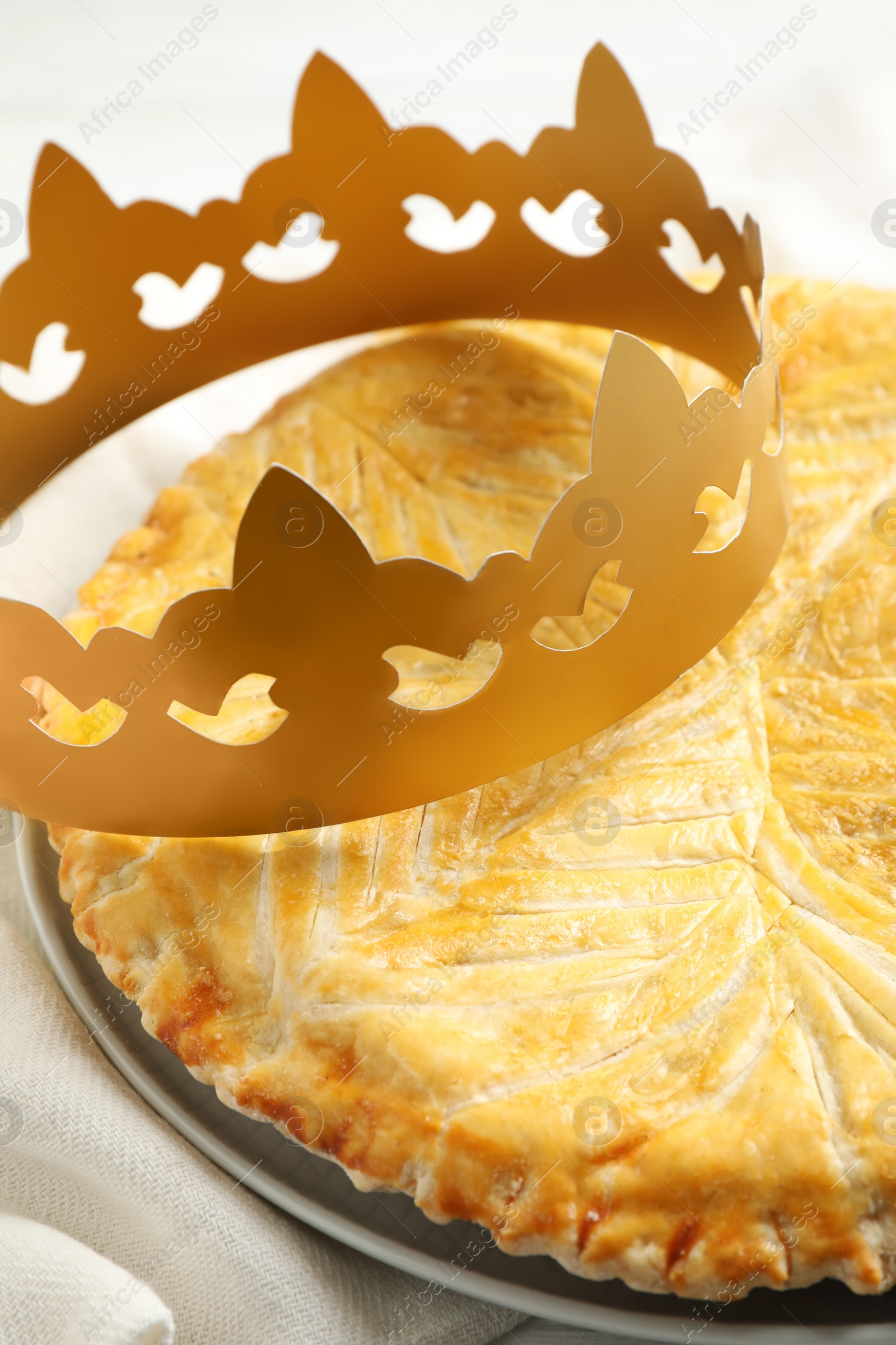 Photo of Traditional galette des Rois with paper crown on table, closeup