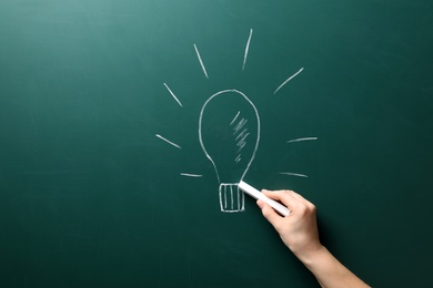 Photo of Woman drawing bulb on chalkboard. Business trainer concept