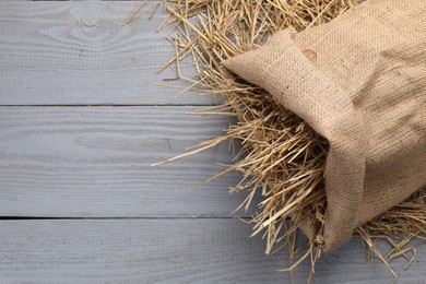 Photo of Dried straw in burlap sack on grey wooden table, top view. Space for text