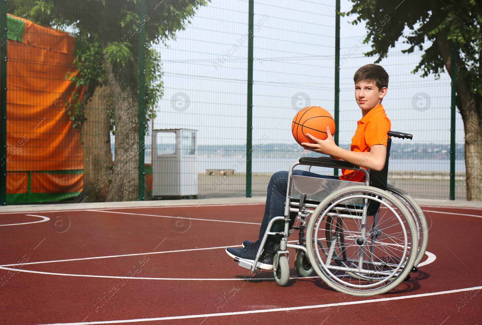 Photo of Disabled teenage boy in wheelchair with basketball ball at outdoor court