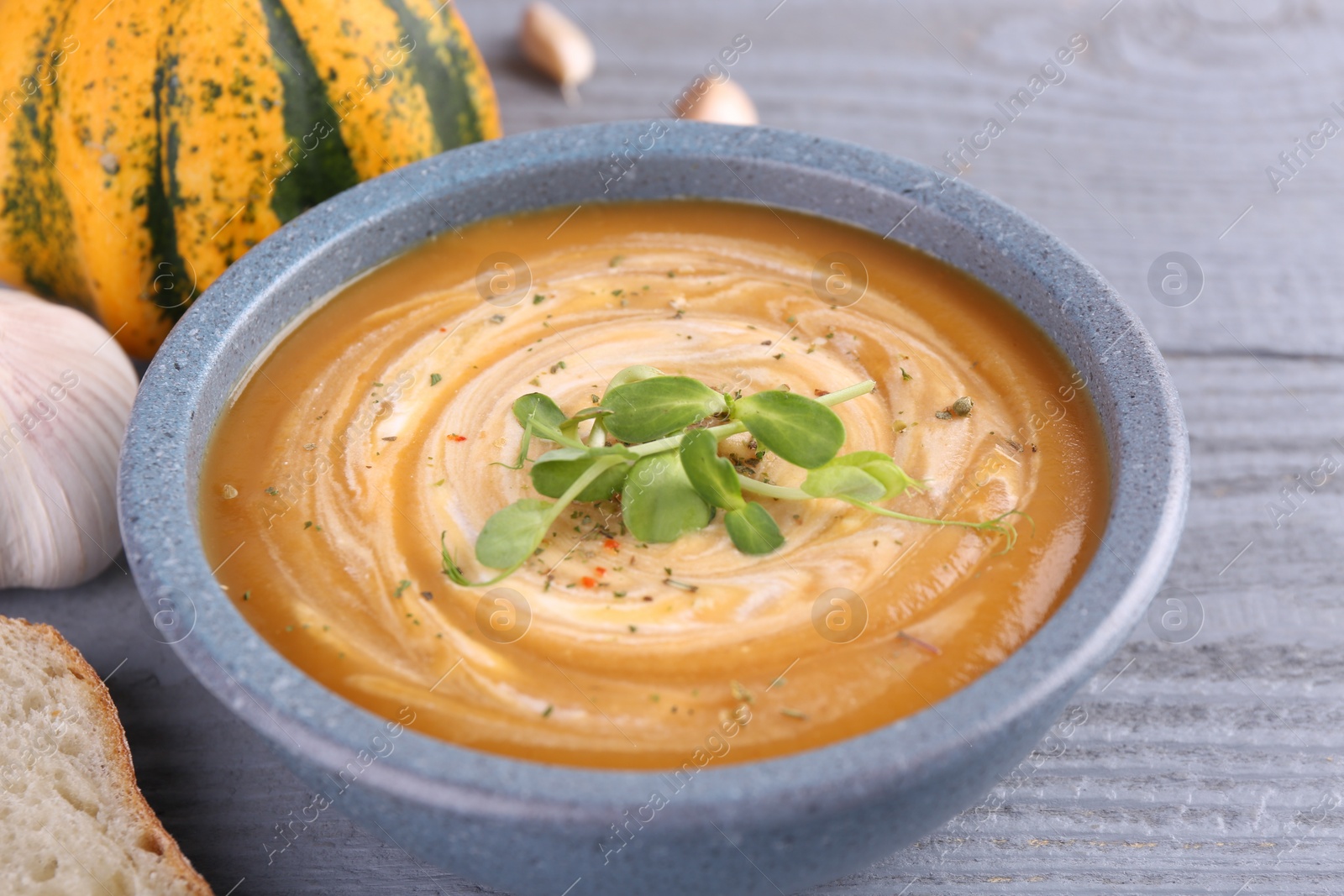 Photo of Tasty pumpkin soup with microgreens in bowl on grey wooden table, closeup