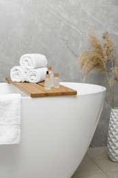 Rolled bath towels and personal care products on tub tray in bathroom