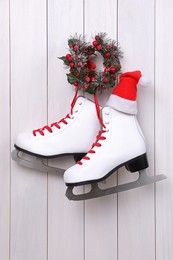 Photo of Pair of ice skates with Santa hat and Christmas wreath hanging on white wooden wall