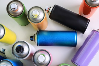 Photo of Cans of different graffiti spray paints on white table, flat lay