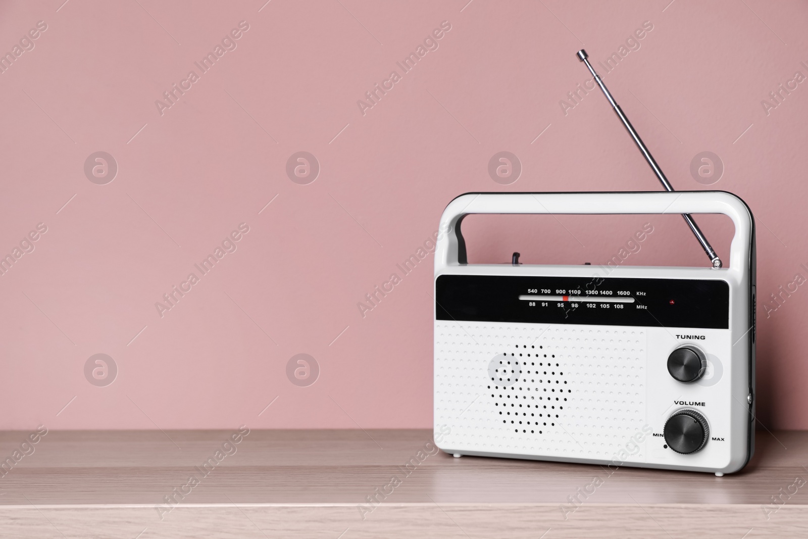 Photo of Retro radio receiver on wooden table against pink background. Space for text