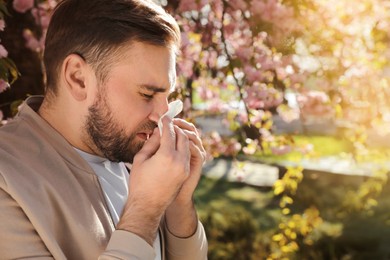 Man suffering from seasonal pollen allergy near blossoming tree outdoors