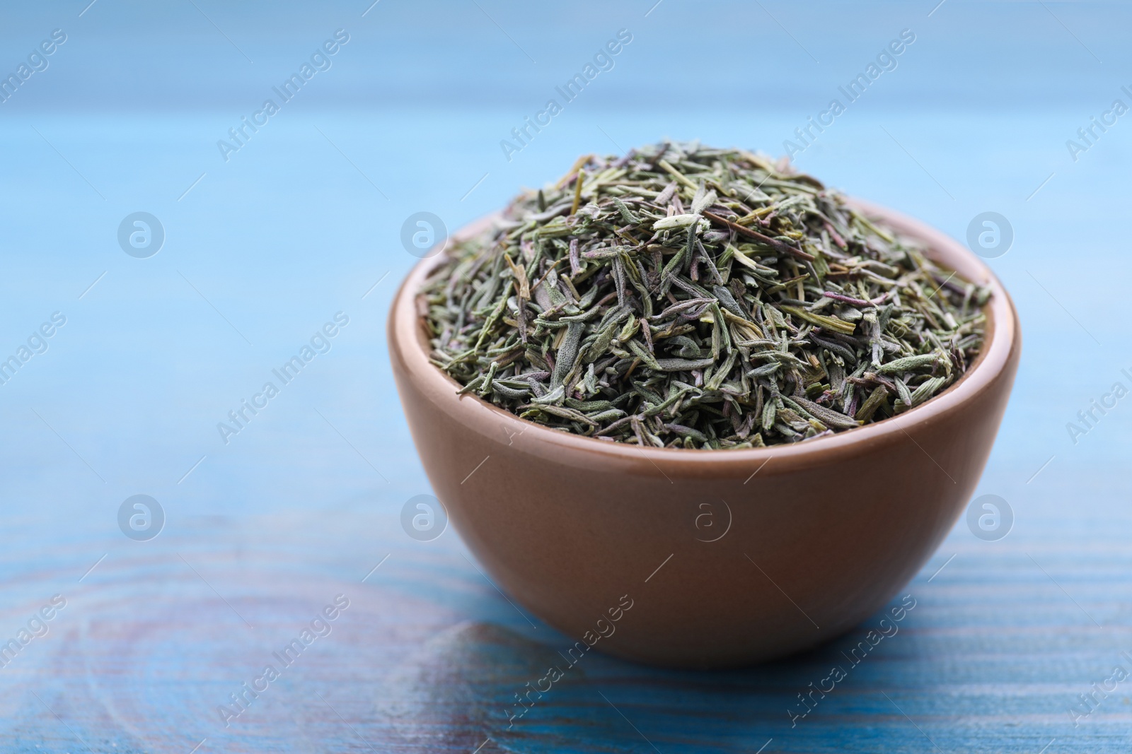 Photo of Ceramic bowl with dried thyme on light blue wooden table, closeup. Space for text
