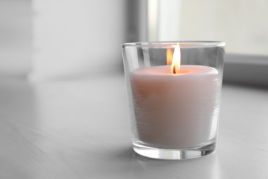 Photo of Beautiful burning wax candle in glass on table