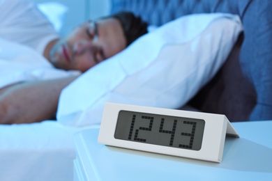 Photo of Young man sleeping in bed and alarm clock on table at night