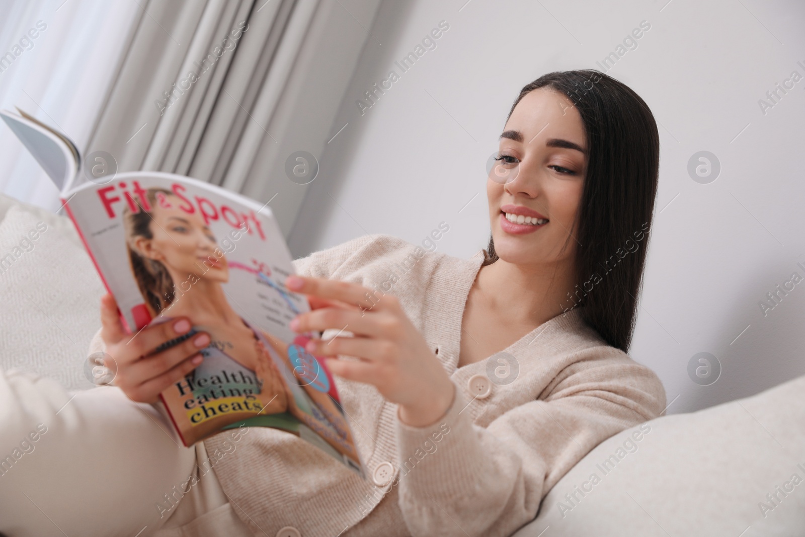 Photo of Young woman reading sports magazine on sofa at home