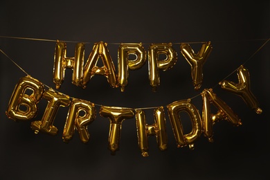 Photo of Phrase HAPPY BIRTHDAY made of golden balloon letters on dark background