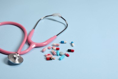 Stethoscope and pills on light blue background, closeup. Space for text