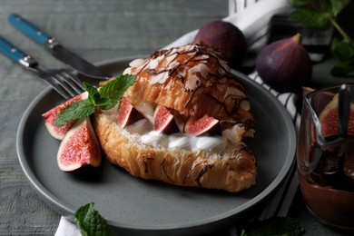 Delicious croissant with figs and cream served on light blue wooden table, closeup