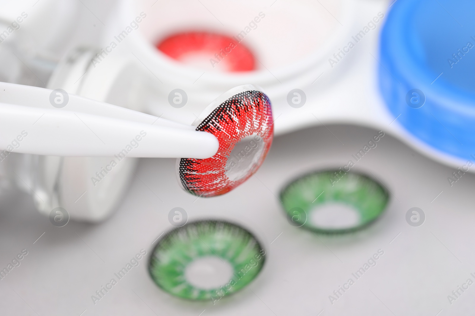 Photo of Tweezers with red contact lens on blurred background, closeup. Space for text