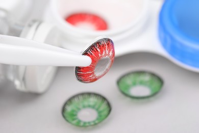 Photo of Tweezers with red contact lens on blurred background, closeup. Space for text