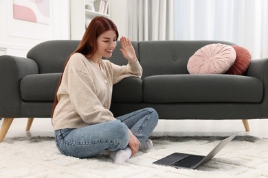 Photo of Happy woman having video chat via laptop on rug in living room