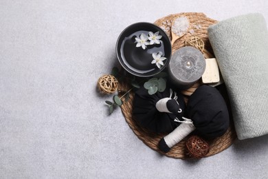 Flat lay composition with herbal massage bags, spa products and flowers on light grey table. Space for text