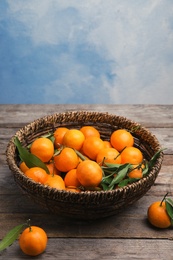 Photo of Fresh ripe tangerines in wicker basket on wooden table. Space for text