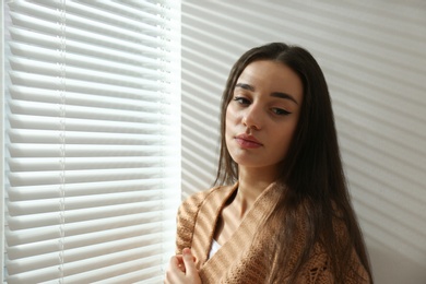 Photo of Young woman near window with Venetian blinds. Space for text