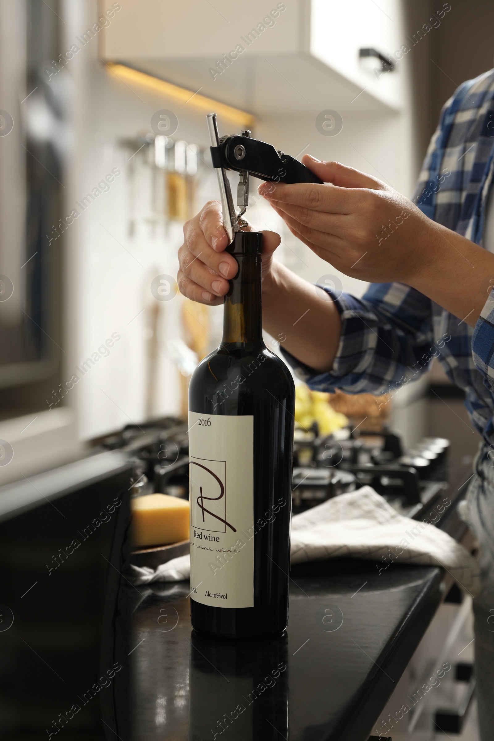 Photo of Woman opening wine bottle with corkscrew at black countertop indoors, closeup