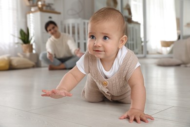 Happy mother watching her cute baby crawl on floor at home