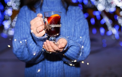 Woman with glass cup of mulled wine and garland at winter fair, closeup