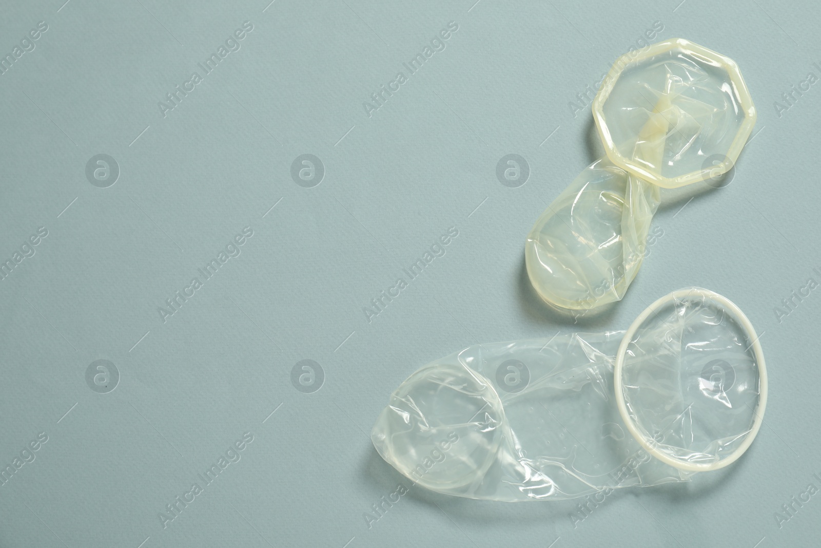 Photo of Unrolled female condoms on light blue background, flat lay with space for text. Safe sex