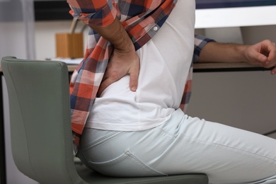 Photo of Young man suffering from back pain in office, closeup