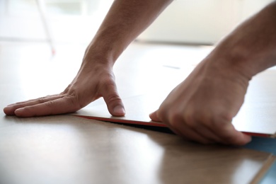 Photo of Worker installing laminated wooden floor indoors, closeup