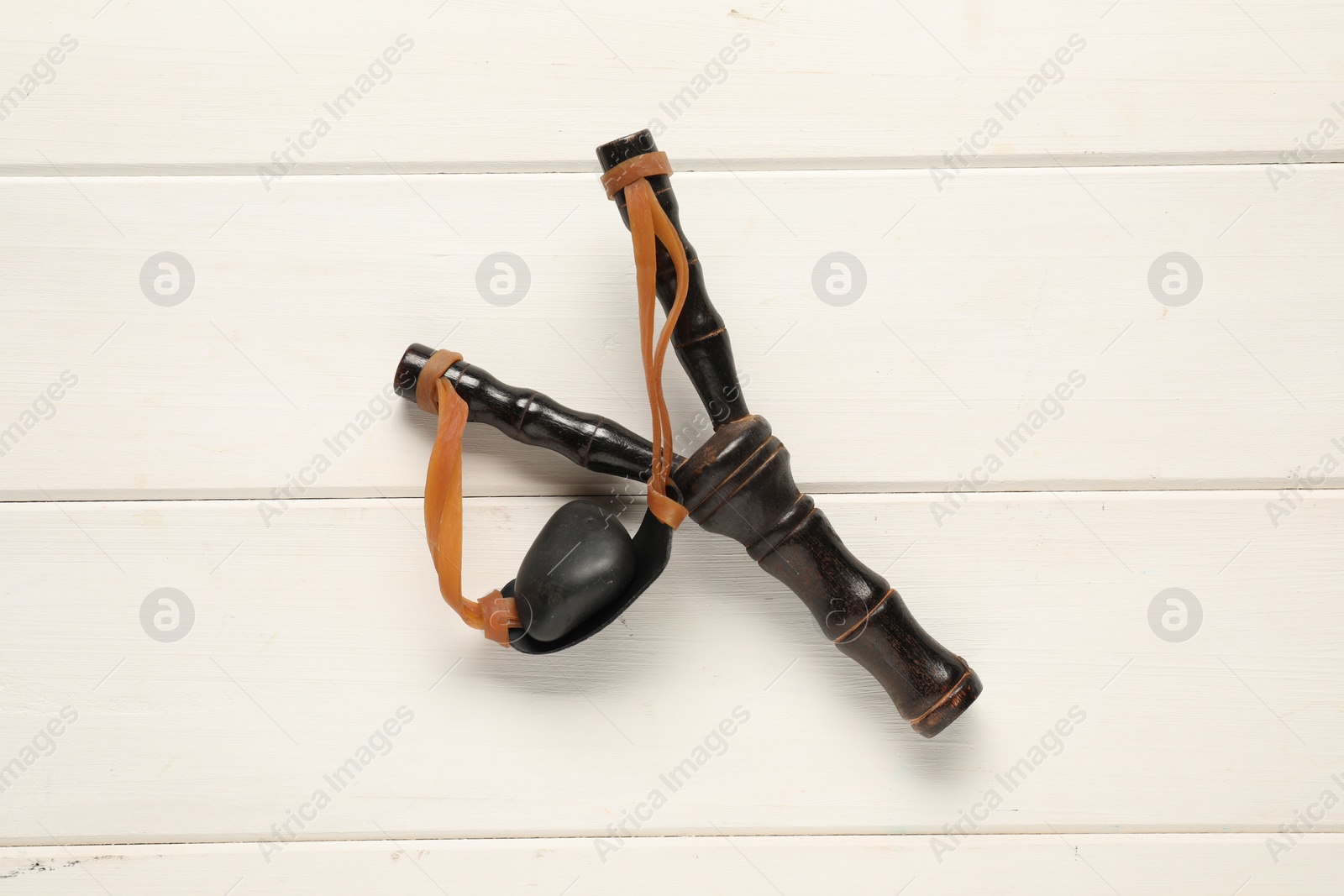 Photo of Black slingshot with pebble on white wooden table, top view