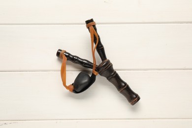 Black slingshot with pebble on white wooden table, top view