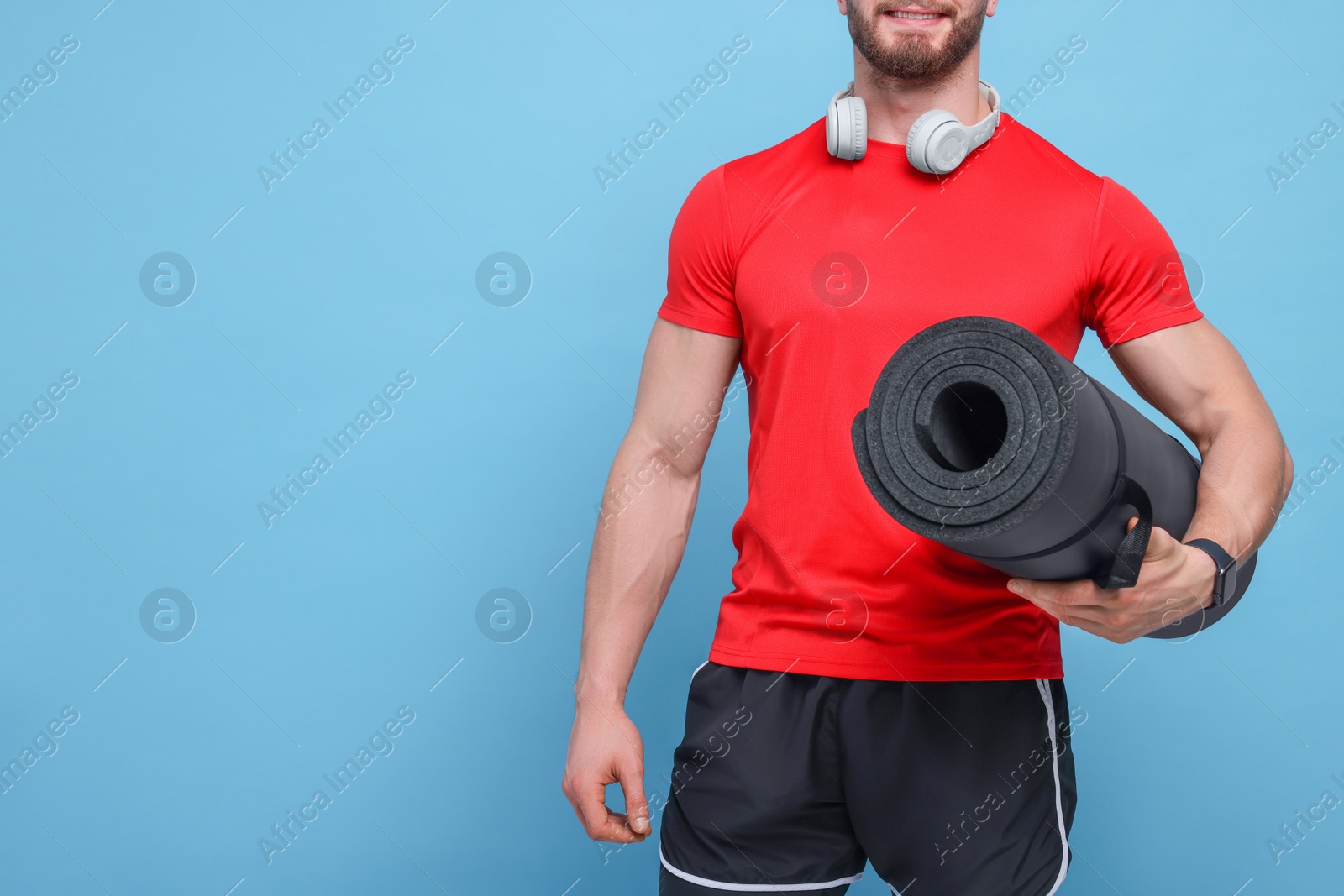 Photo of Man with fitness mat and headphones on light blue background, closeup. Space for text