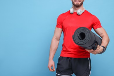 Photo of Man with fitness mat and headphones on light blue background, closeup. Space for text