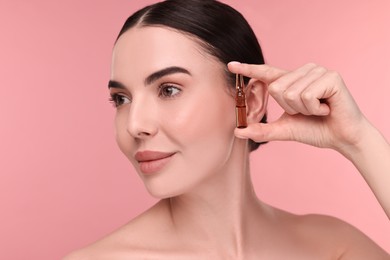 Photo of Beautiful young woman holding skincare ampoule on pink background